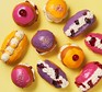 A selection of yellow, purple and pink iced buns filled with cream & jam